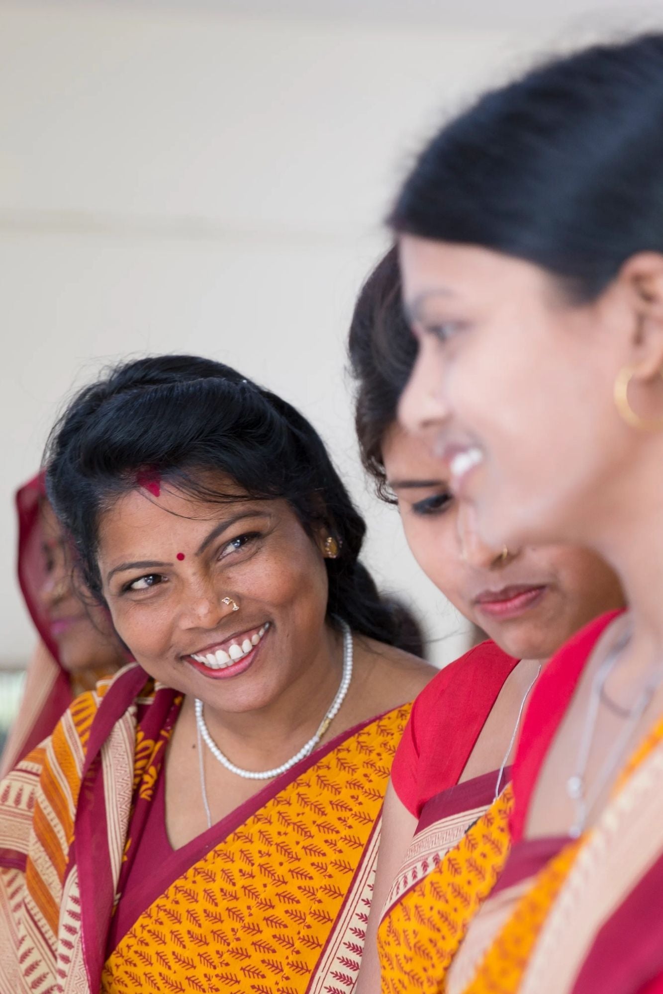 Group of Indian women in traditional attire smiling and interacting.